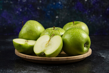 Whole and sliced ripe green apples on wooden plate
