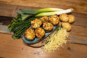 A selection of delicious Fish Pie Potato Skins topped with cheese and garnish on a wooden kitchen table background surrounded by the ingredients used to create the dish