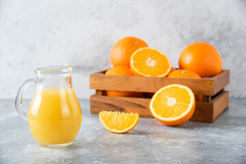 A glass pitcher of juice with fresh orange fruits on stone background