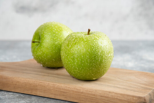 Two whole green apples on wooden plate on marble background