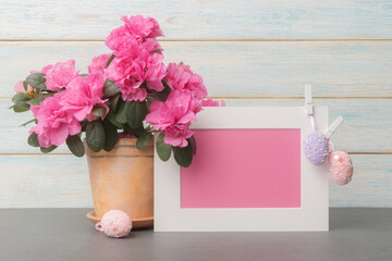 Pink flowers and blank card in white frame with Easter eggs over wooden background