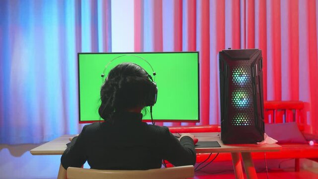 Young Asian Gamer Girl Put On Black T-Shirt Focused To Green Screen While Playing Video Game
