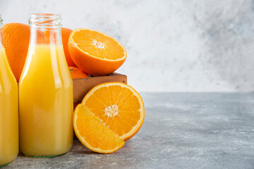 A glass pitcher of juice with fresh orange fruits on stone background