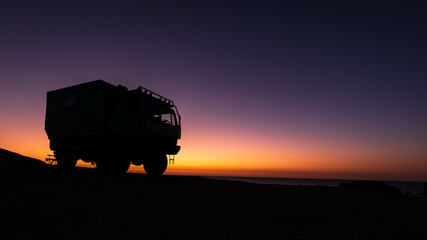Silhouette of RV camping truck in front of colorful sunset, Sahara Desert, Morocco