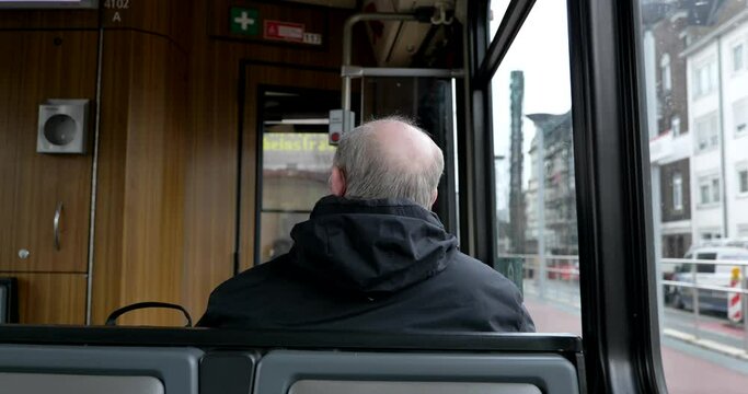 Interior and selective focus, back of old male passenger with hair loss problem wear face protection mask and sit in light rail tram or train in Germany during epidemic of COVID-19 virus.