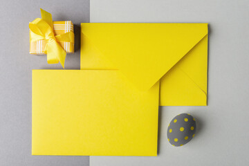 Yellow envelope with blank card, decorative egg and gift box on grey background