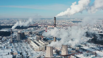 Aerial view snowy industrial area, drone flies over thermal power plant in winter. City factories on frosty sunny day. Industrial district from above, smoke pipes, white clouds of steam from pipes