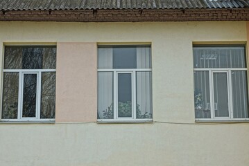 a row of three white windows on a brown concrete wall of a building on the street
