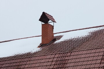 one red brick chimney on a brown tiled roof of a private house in white snow on a winter street...
