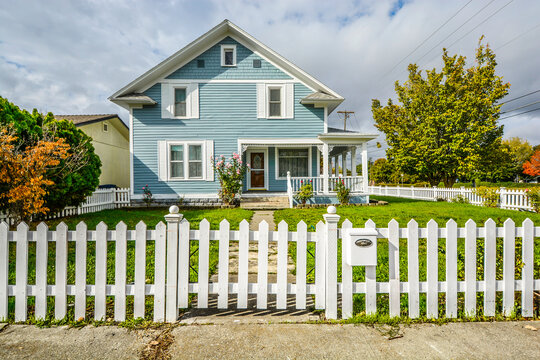 Front view of a Victorian style home with a white picket fence, wraparound porch and garden in the Pacific Northwest of the USA