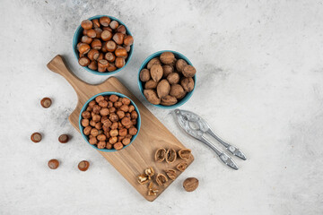 Bowls of walnuts, hazelnuts and kernels on wooden cutting board