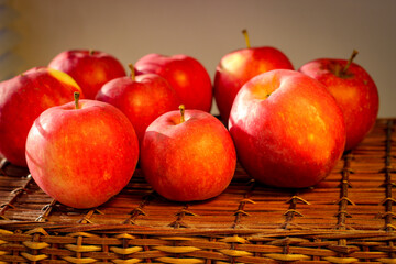 Several ripe red apples stand on a wicker basket illuminated by rays of the sun