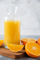 Glass pitcher of juice with fresh orange fruits on a wooden board