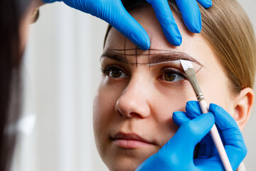 A woman permanent makeup artist draws a sketch of the eyebrows on the face of her client.