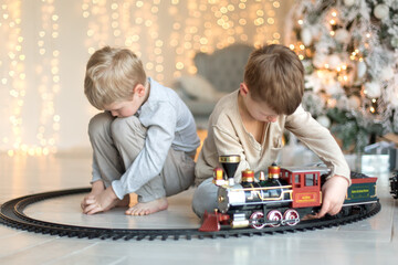 Two cute little boys are playing near the Christmas tree in a red train. Family Christmas and New Year