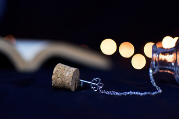 Key necklace stacked in a cork. Chain getting out from a bottle. Book out of focus. 