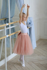 a ballerina girl in a tutu and pointe shoes standing by a ballet stick