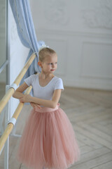 A cute ballerina girl in a full skirt and pointe shoes standing near a ballet stick. Children and ballet. Workout