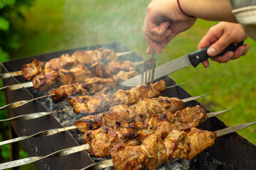 Cooking grilled meat on the grill, hands with a knife and fork, cut a piece of meat on a skewer.