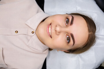 Woman with permanent makeup tattoo on her eyebrows. Close-up beautician makes makeup applies a...