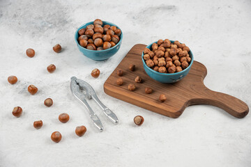 Two blue bowls of shelled hazelnuts and kernels on marble background
