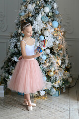A small ballerina in a pointe near the Christmas tree holding a nutcracker Nutcracker . New Year's gifts