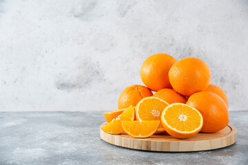 A wooden board full of juicy slices of orange fruit on stone background