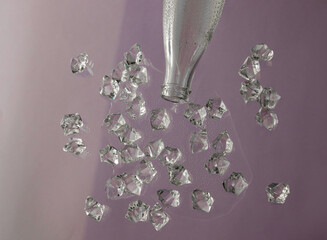 Bottled water spilled on a glass table. Pieces of ice in water and a neck in a bottle on a lilac background