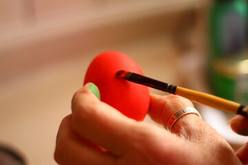 A woman's hand paints an Easter egg. Preparing Easter decorations on Multicolor background. 
