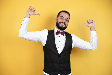 Young man with beard wearing bow tie and vest looking confident with smile on face, pointing oneself with fingers proud and happy.