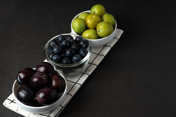 Black and green plums in white ceramic saucer