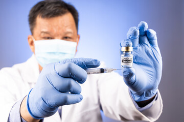 Close-up and focus on Covid-19 vaccine vial and syringe held by Asian medical doctor with medical glove in background