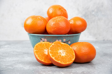 Whole and slice juicy fresh orange fruits in a bowl placed on a stone background