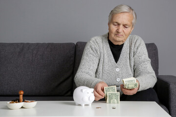 Elderly woman counting last coins from piggy bank, sitting depressed and worried at home. Concept of savings, insurance and retirement.