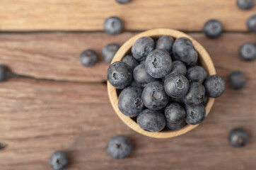 Top view blueberry in a wood bowl and heap on the brown wooden