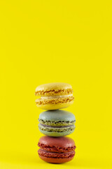 A vertical shot of three colorful macaroons stacked on top of one another with a vibrant yellow background and copy space.