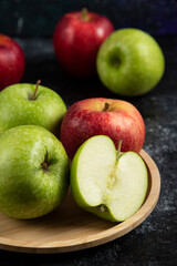 Whole and sliced green and red apples on wooden plate