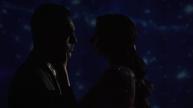 A young couple stands in the shade and tries to kiss, amid laser projection stars