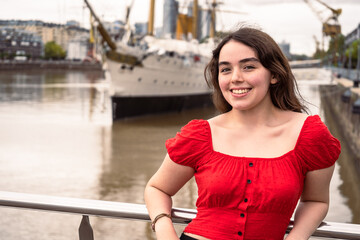 Smiling Latin American teenage woman with beautiful teeth leaning on a railing on a cloudy day.