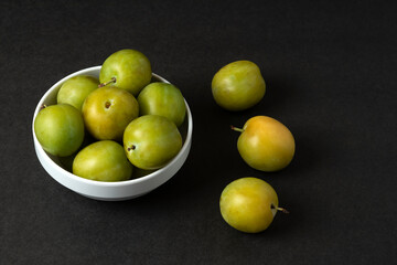 Green plums in a white ceramic saucer