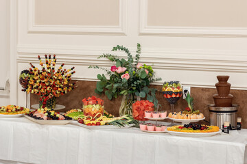Beautifully decorated wedding table. Table setting. Tangerines, grapes, blueberries, kiwi and other fruits and berries, cookies and all sorts of goodies.