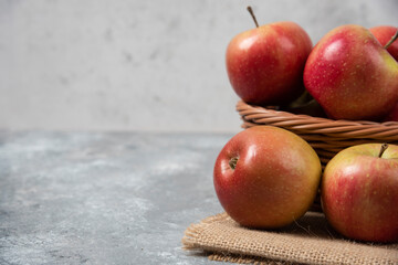 Wicker basket of ripe shiny apples on marble surface