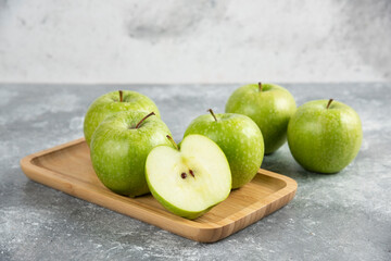 Bunch of whole and sliced green apples on wooden plate