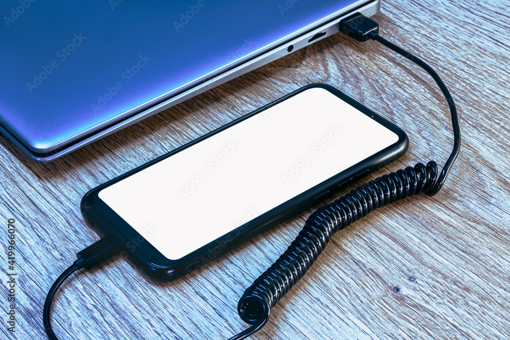 Poster mock-up of a smartphone with a white screen close-up being charged from a laptop on the background o