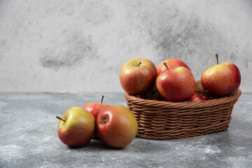 Wicker basket of red juicy apples on marble surface