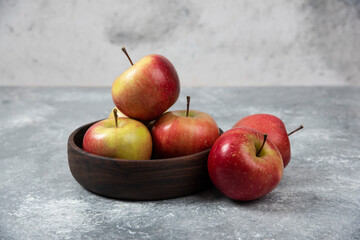 Wooden bowl of fresh tasty apples on marble surface