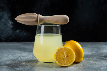 A glass cup of lemon juice and wooden reamer