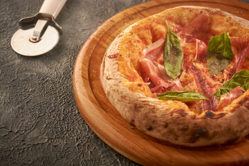 pizza recien salida del horno sobre una tabla de madera en una mesa rustica negra y un cortador 