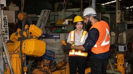 Female mechanic engineer or worker with hardhat and safety gears is working with her supervisor in a factory checking the function of a system