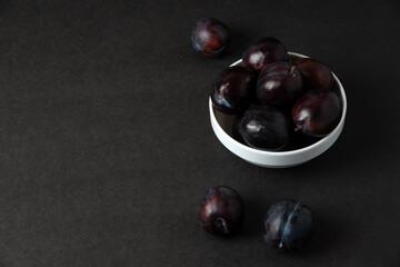 Black plums in white ceramic saucer on black background